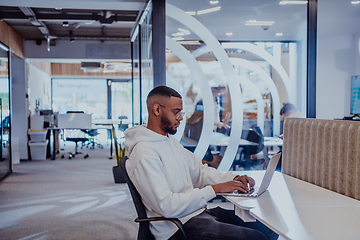 Image showing In a modern office setting, an African American businessman is diligently working on his laptop, embodying determination, ambition, and productivity in his professional environmen