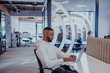 Image showing In a modern office setting, an African American businessman is diligently working on his laptop, embodying determination, ambition, and productivity in his professional environmen