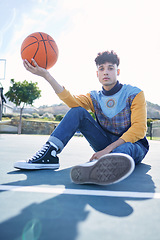 Image showing Basketball, court and portrait of a man model sitting on the ground with stylish, trendy and cool clothes. Sports, relax and guy from Canada holding a ball on outdoor training field in the urban city