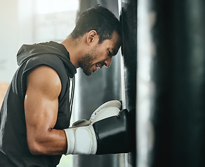 Image showing Strong, sweaty and fit male boxer resting while doing a cardio workout with a punching bag at gym. Sporty, active and determined athlete looking tired while exercising at a sports center for fitness.