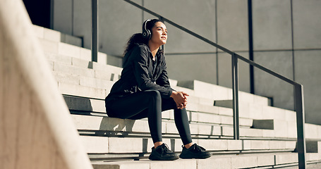Image showing Runner woman, headphones and smile on stairs for music, ideas and relax in city, workout or training. Girl, thinking and happy on steps with audio streaming subscription with peace in summer sunshine