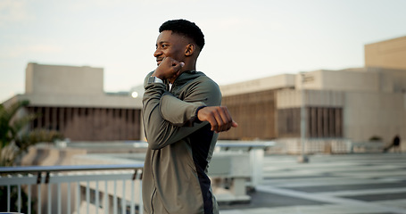 Image showing Black man, fitness and stretching on rooftop in city for workout, training or outdoor exercise. Happy African male person, runner or athlete in body warm up or arm stretch getting ready in urban town