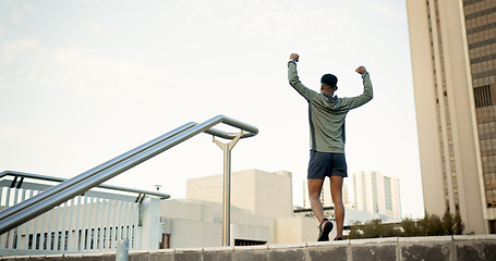 Image showing Man, fitness and celebration in city with fist pump for achievement, workout or success in outdoor exercise. Rear view of male person, runner or athlete with hands up in victory for training in town