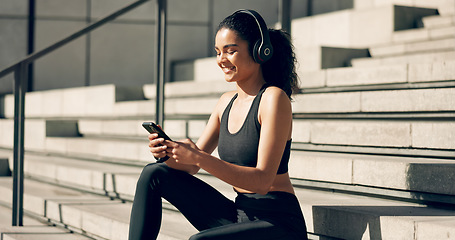 Image showing Runner girl, headphones and phone on stairs with music, smile and relax in city, workout and training. Woman, smartphone and sitting with audio streaming subscription with typing, social media or app
