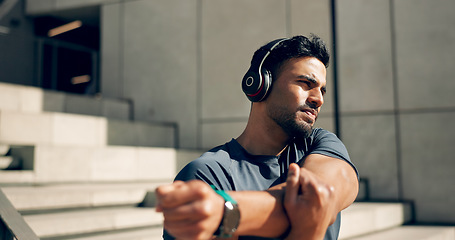 Image showing Fitness, headphones and man stretching arms on stairs in city, workout and exercise for body health. Music, serious athlete and person warm up on steps in urban town, listening to audio and thinking