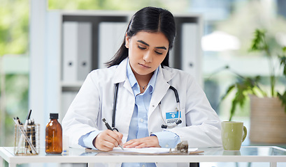 Image showing Doctor writing a prescription or recommending medication letter while sitting at her desk. Professional female GP, surgeon or physician writing a medical file and report in clinic alone in a office