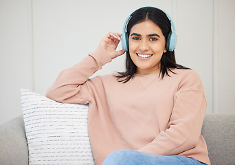 Image showing Happy, relaxed and beautiful female with headphones listening to music sitting on the couch at home. Portrait of a young female streaming a podcast online and enjoying relaxing in the living room