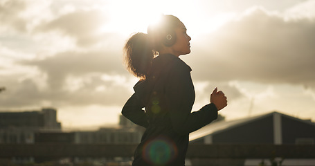 Image showing Athlete, morning and running in city with headphones for fitness, workout and marathon training music. Sun lens flare, woman or exercise podcast in Brazil for cardio wellness, clouds or sports radio