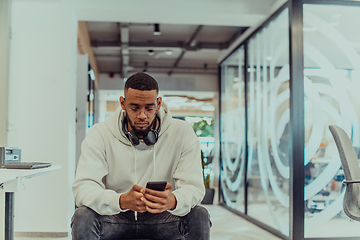 Image showing African American businessman wearing headphones while using a smartphone, fully engaged in his work at a modern office, showcasing focus, productivity, and contemporary professionalism