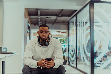 Image showing African American businessman wearing headphones while using a smartphone, fully engaged in his work at a modern office, showcasing focus, productivity, and contemporary professionalism