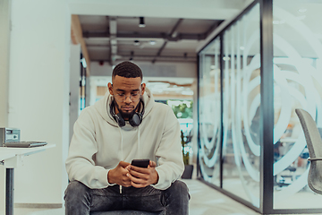 Image showing African American businessman wearing headphones while using a smartphone, fully engaged in his work at a modern office, showcasing focus, productivity, and contemporary professionalism