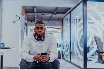 Image showing African American businessman wearing headphones while using a smartphone, fully engaged in his work at a modern office, showcasing focus, productivity, and contemporary professionalism