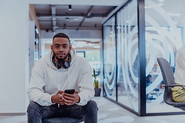 Image showing African American businessman wearing headphones while using a smartphone, fully engaged in his work at a modern office, showcasing focus, productivity, and contemporary professionalism