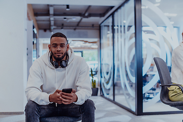 Image showing African American businessman wearing headphones while using a smartphone, fully engaged in his work at a modern office, showcasing focus, productivity, and contemporary professionalism