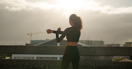 Image showing Woman, stretching and fitness in city for workout, exercise or outdoor training in sunset. Rear view of female person, runner or athlete in body warm up or arm stretch getting ready in an urban town