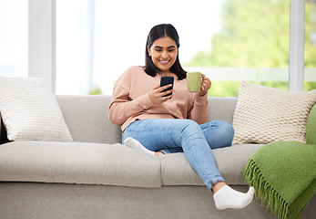 Image showing Rest, relaxation and carefree with a young woman typing on a phone, drinking coffee and comfortable on the sofa at home. Relaxed female browsing social media or typing a message with a cup of tea