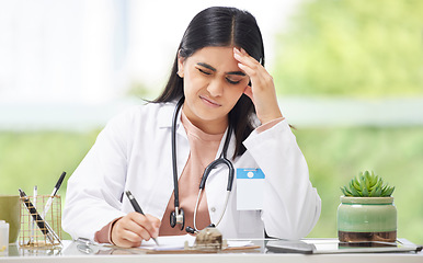 Image showing Headache, stress and burnout medical doctor working in hospital, looking in pain and writing in a book while sitting in office at clinic. Tired, unhappy and professional female healthcare worker