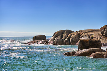 Image showing Scenic view of nature, rocks and calm ocean water on a sunny day in Summer, with a beautiful blue sky in the background. Sea waves breaking close to the shore of the beach.