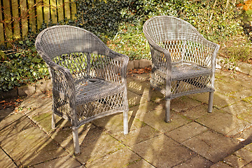 Image showing Woven armchairs outside in a rustic garden with green plants for relaxing after gardening. Yard landscape with two wooden chairs in nature in a backyard patio to enjoy the sun on a warm winter day