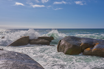 Image showing A beautiful coastline with waves and rocks in the sea on a sunny, beach day. An ocean view of the water and a blue sky background in summer. Outdoor scenery of a relaxing seaside landscape in nature.