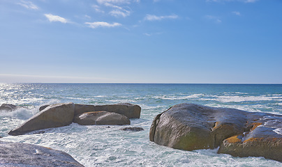 Image showing Big rocks in the ocean or sea water with a blue sky background. Beautiful landscape with a scenic view of the beach with boulders on a summer day. Relaxing scenery of the seaside or nature