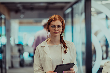 Image showing A young business woman with orange hair self-confident, fully engaged in working on a tablet, exuding creativity, ambition and a lively sense of individuality