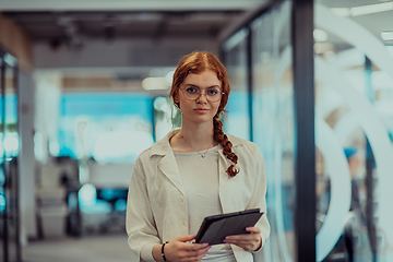 Image showing A young business woman with orange hair self-confident, fully engaged in working on a tablet, exuding creativity, ambition and a lively sense of individuality