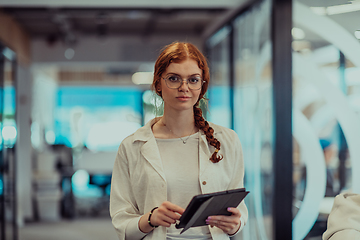 Image showing A young business woman with orange hair self-confident, fully engaged in working on a tablet, exuding creativity, ambition and a lively sense of individuality