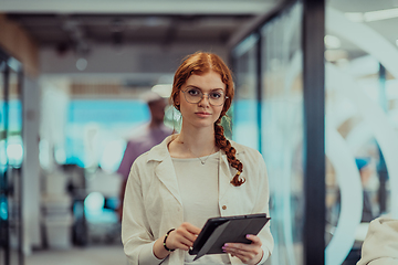 Image showing A young business woman with orange hair self-confident, fully engaged in working on a tablet, exuding creativity, ambition and a lively sense of individuality