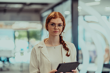Image showing A young business woman with orange hair self-confident, fully engaged in working on a tablet, exuding creativity, ambition and a lively sense of individuality