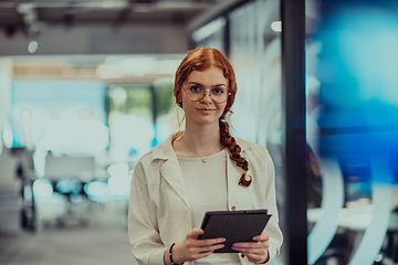 Image showing A young business woman with orange hair self-confident, fully engaged in working on a tablet, exuding creativity, ambition and a lively sense of individuality