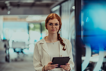 Image showing A young business woman with orange hair self-confident, fully engaged in working on a tablet, exuding creativity, ambition and a lively sense of individuality