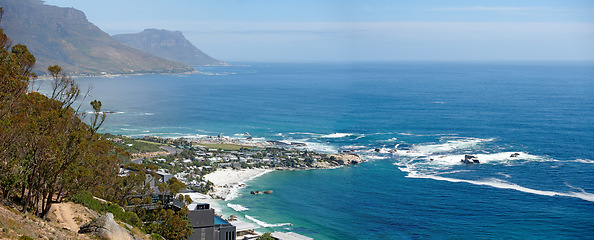 Image showing Panorama of a mountain coastline with quiet ocean against a blue sky in South Africa from above. Scenic wallpaper of a serene landscape of calm waves near Camps Bay with a peaceful sea view.