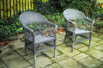 Image showing Cozy garden area for coffee and reading outside in the warm summer. Two grey woven lawn chairs on a stone patio outside in an overgrown backyard. Old outdoor furniture in a private location to relax