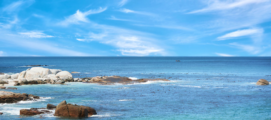 Image showing Boulders at a beach against a cloudy blue sky background with copy space. Calm and majestic ocean across the horizon and rocky coast. Scenic landscape of the sea for a summer holiday or getaway