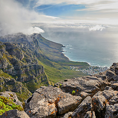 Image showing Aerial view of a majestic mountain landscape, an ocean and a city in a valley during a cloudy day. Beautiful scenery of a cloudscaped sky above a rocky terrain with the sea below with copy space