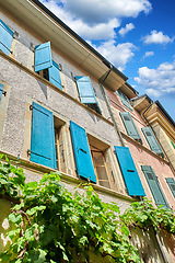 Image showing The classical architecture of a tall residential building with overgrown green plants on the wall. The exterior of an old apartment block on a sunny day. Bottom view of antique city flats