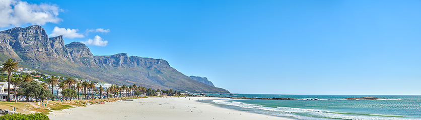 Image showing Quiet and calm beach and ocean with sandy shore and palm trees. Scenic seascape of the Twelve Apostles mountain under a blue sky in Cape Town. A beautiful holiday destination for travel and tourism