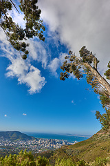 Image showing Beautiful scenic view of a coastal city from a mountain peak with trees and plants against a cloudy blue sky background. Magnificent panoramic of a peaceful landscape at the sea to explore and travel