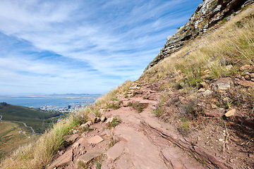 Image showing Scenic of a rocky mountain slope with view of a coastal city by the sea and cloudy sky background with copyspace. Rugged landscape on a cliff with hiking trail on Lions Head, Cape Town, South Africa