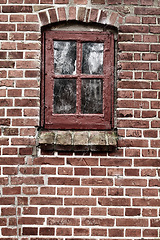 Image showing Old dirty window in a red brick house or home. Ancient casement with red wood frame on a historic building with clumpy paint texture. Exterior details of a windowsill in a traditional town or village