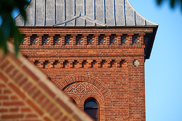 Image showing Closeup of a red face brick church steeple against a blue sky. Tall infrastructure and tower used to symbolise faith and Christian or Catholic devotion. Architecture of a built structure outside