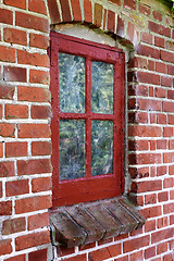 Image showing Old dirty window in a brick wall house or home. Ancient casement with red wood frame on a historic building with a clumpy paint texture. Exterior details of a windowsill in a traditional country town