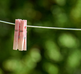 Image showing Closeup of washing line with pins hanging outside against a bokeh green background. Empty clothesline with plastic clothes peg in a backyard on laundry day with copy space for domestic chores