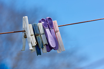 Image showing Old washing line with broken pins hanging outside against a blurred blue background. Brown clothesline with different plastic pegs in a backyard on laundry day with copy space for domestic chores