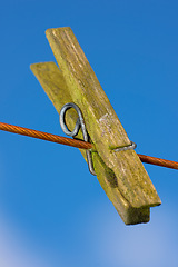 Image showing Closeup of one clothes peg hanging on an empty laundry line outside in a garden. A clothing pin is a tool to hang up clothes outside to dry while doing housework and chores. Zoom of a wooden peg