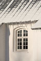 Image showing Empty building with ice damming on the roof on a cold winter day. The exterior of a home or house with snow on the rooftop on a sunny afternoon. Frost on a historic church in a village