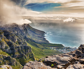 Image showing Aerial view of clouds rolling over Table mountain in Cape town, South Africa with copyspace. Beautiful landscape of green bushes and rocky terrain on misty morning, calming view of the ocean and city
