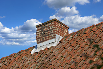 Image showing Red brick chimney designed on slate roof of house building outside against blue sky with white clouds background. Construction of exterior escape chute built on rooftop for fireplace smoke and heat