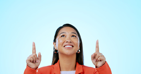 Image showing Business woman, face and pointing up in studio for advertising choice, decision and information about us on blue background. Happy asian worker, thinking and presentation of mockup ads, ideas or deal